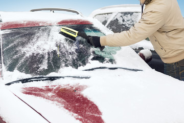 man cleaning snow from car windshield with brush