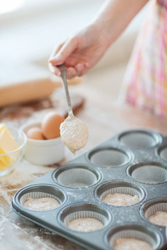 close up of hand filling muffins molds with dough