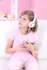 Naklejka premium Little girl sitting on sofa and listening music in room
