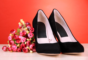 Obraz na płótnie Canvas Beautiful black female shoes and flowers on red background