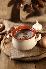 Mushroom soup in pot, on wooden table, on sackcloth background