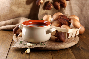 Mushroom soup in pot, on wooden table, on sackcloth background