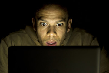 Man looking in shock at his laptop late at night - 61740917