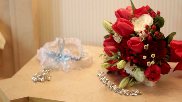bridal bouquet of red roses and rings on the table