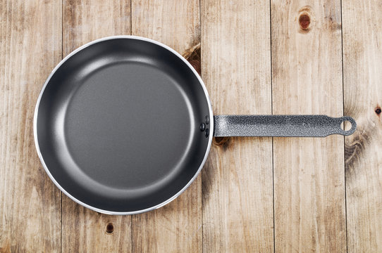 Frying pan on wooden table background. View from above