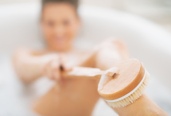 Closeup on young woman in bathtub using body brush