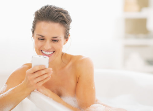 Young woman in bathtub writing sms