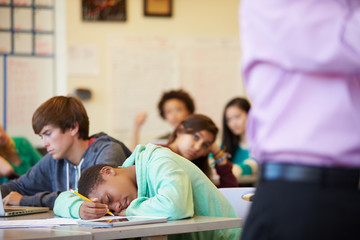 Bored High School Pupil Slumped On Desk In Classroom - Powered by Adobe