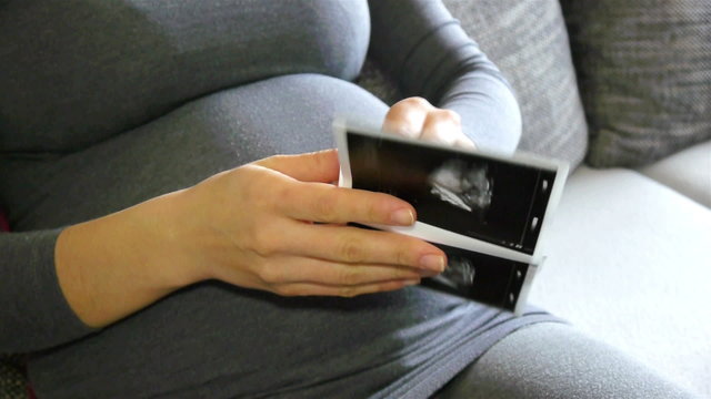 Pregnant woman holding ultrasound images