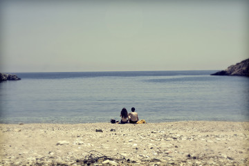 Young couple sitting on the beach and looking at sea