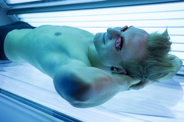 Man in solarium enjoying sunbathing on tanning bed - obrazy, fototapety, plakaty