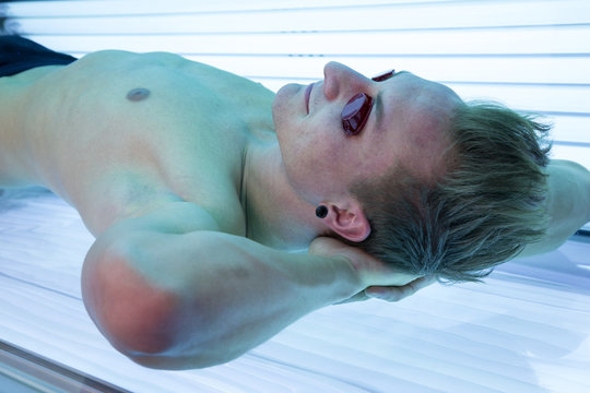 Man with sunglasses on tanning bed in solarium