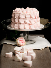 Scalloped pale pink cake on glass stand next to rose and marshma
