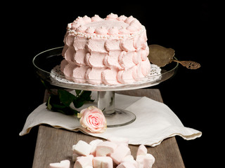 Scalloped pale pink cake on glass stand next to rose and marshma