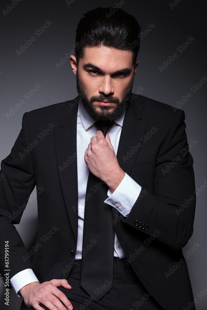 Poster seated young fashion man fixes his tie