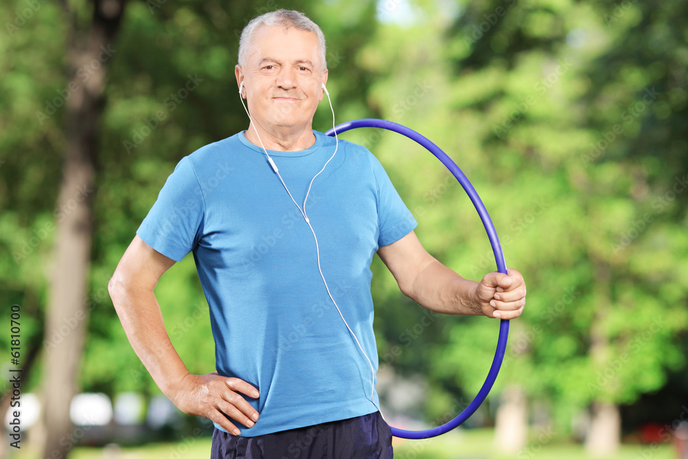 Sticker Smiling mature man with headphones holding a hula hoop in park