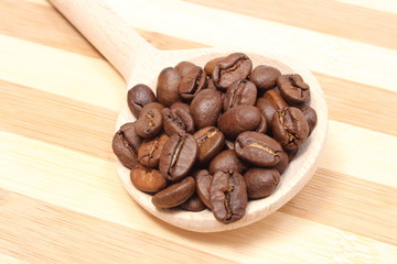 Heap of coffee on wooden spoon. Wooden background