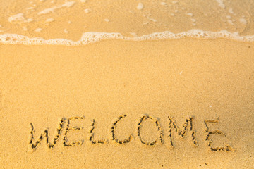 Welcome, written in sand on beach texture, soft wave of the sea.