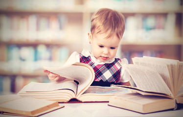 Happy baby girl reading a book in a library