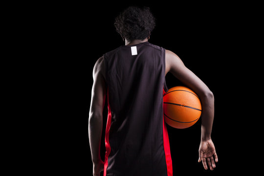 Rear view of a basketball player holding a ball against dark bac