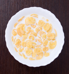 Corn flakes with milk in bowl on a brown wooden background