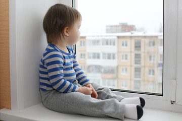 sad baby sitting on window sill