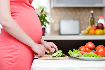 Obraz na płótnie Canvas pregnant woman with knife on kitchen cuts cucumber