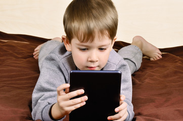 little boy 5 years lying and playing on a tablet