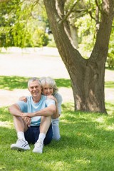 Fototapeta premium Smiling mature couple sitting on grass at park