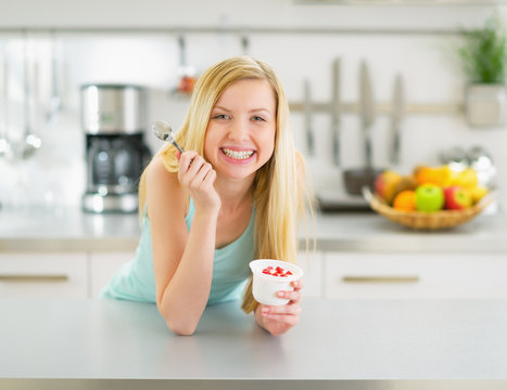 Happy young woman eating yogurt in kitchen