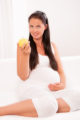 Obraz na płótnie Canvas Beautiful pregnant woman on sofa eating an apple