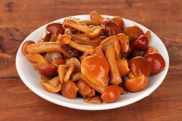 Marinated mushrooms in saucer on wooden table