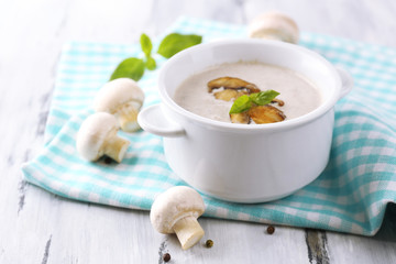 Mushroom soup in white pot, on napkin,  on wooden background