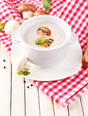 Mushroom soup in white pot, on napkin, on wooden background