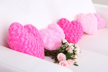Pink hearts shaped pillow and flowers on white sofa