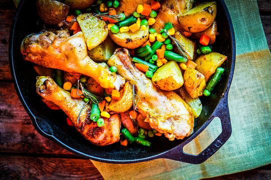 Oven baked chicken with potatoes and vegetables on wooden backgr