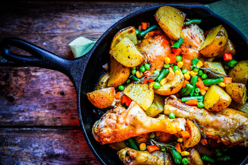 Oven baked chicken with potatoes and vegetables on wooden backgr