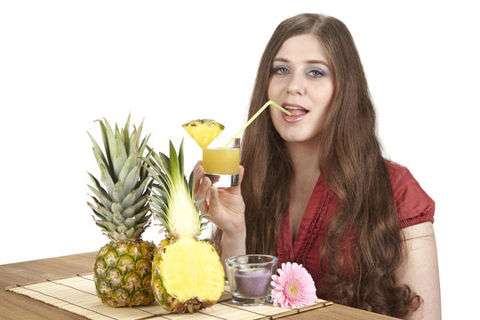 Junge Frau mit einem Glas Ananassaft und Ananas am Esstisch