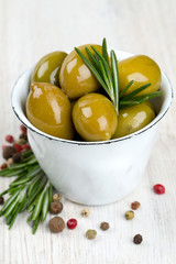 green olives in a metallic cup on wooden surface