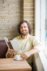 Man With Book And Coffee Cup Sitting In Cafeteria
