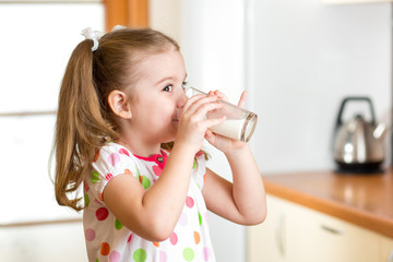 child girl drinking yogurt or milk in kitchen