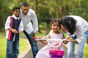 indian family guiding little daughter to cycle