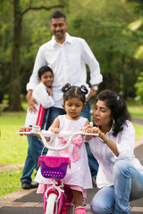 indian family guiding little daughter to cycle