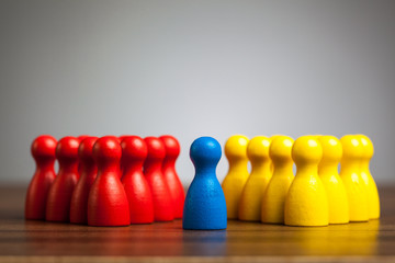 Single blue pawn figure between red and yellow groups - obrazy, fototapety, plakaty