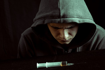 Grunge image of a depressed drug addict looking at a syringe