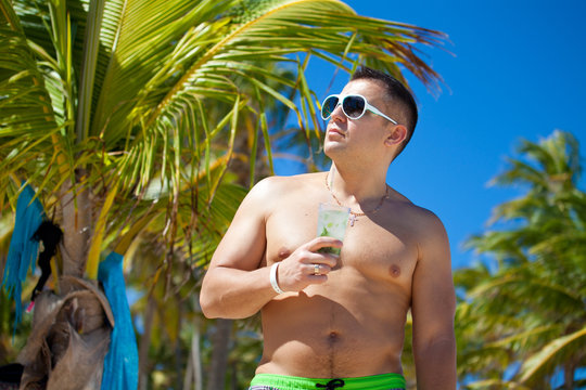 Attractive young man in the beach, having a drink