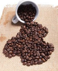 white cup with coffee beans on burlap background.