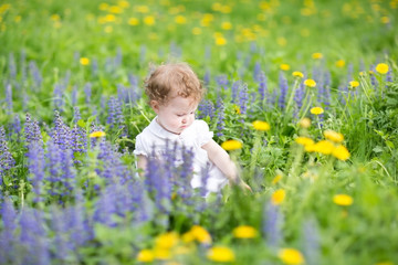 Adorable baby girl playing in a blooming summer garden