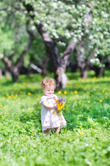 Funny little girl playing with flowers in a apple graden