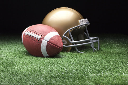 Football and helmet on grass against dark background